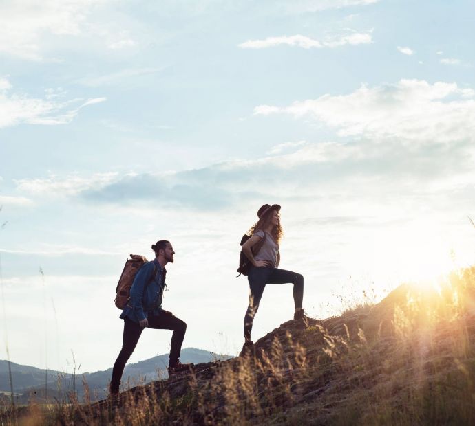 Allers Landing Two people hiking uphill at sunset with backpacks, surrounded by nature and distant mountains.