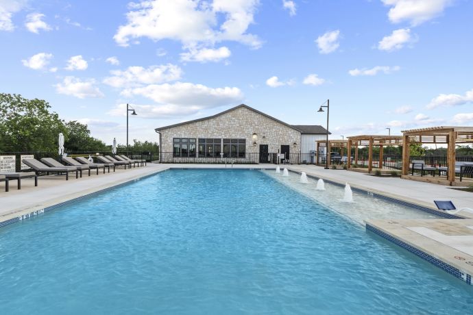 Allers Landing Outdoor swimming pool with lounge chairs, water jets, and a clubhouse under a partly cloudy sky.